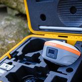 A CHCNAV GNSS Receiver with a grey body and orange band sits in a black foam-lined yellow hard case available to buy or hire from Tri-Site. Buy brand new or second-hand for the best price.